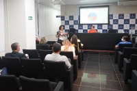 Um mulher em pé com uma tela atrás apresentanto um gráfico para platéia