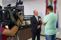 Homem de terno escuro, cabelos brancos, falando com homem forte de camisa verde