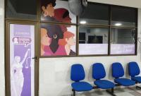 Fachada da ouvidoria da mulher adesivada com cartaz na porta com a deusa têmis na cor lilás clara e, ao fundo, lilás escuro; na janela, adesivação com as imagens de mulheres de várias etnias.