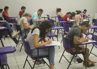 IMAGEM DE CANDIDATOS SENTADOS EM UMA SALA DE AULA FAZENDO AS PROVAS DO CONCURSO DO TRT-19. A foto foi registrada do lado direito.