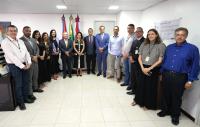 Foto geral dos participantes das 14 pessoas que participaram da reunião, com o presidente do TRT-19 ao centro e, atrás, as bandeiras do Brasil, de Alagoas e do TRT-19