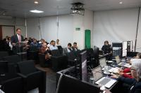 Auditório com várias pessoas em frente a uma bancada. Há um homem de peleclara falando para mulheres e homens em uma bancada
