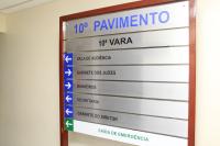 Placa indicativa na cor prata com moldura de madeira, há inscrições com letras nas cores azul e preta. 