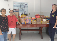 Três pessoasl em pé defronte a uma mesa repleta de alimentos doados
