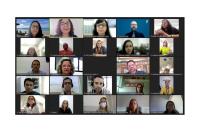 Palestra telepresencial. Há uma tela de computador com rostos de homens e mulheres vendo a palestrante fazendo apresentação.a