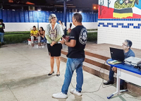 Um mulher morena, de cabelos curtos e brancos em pé conversando com um homem em pé de camisa preta