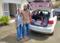 Foto com duas pessoas em pé, uma mulher e um homem. À direita, um carro branco.