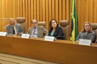 Duas mulheres bem vestidas e dois homens de terno em uma bancada de madeira