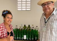 NA FOTO, UMA MULHER COM BLUSA SE XADREZ VERMELHA E BRANCA E UM HOMEM COM BLUSA DE XADRE COM LINHA PRETAS E BRANCAS USANDO UM CHAPÉU DE PALHA