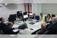Foto de uma audiência de conciliação, com cinco advogados usando ternos escuros; um juiz usando terno azul-marinho, um servidor de camisa amarelo claro e uma advogada usando blusa branca