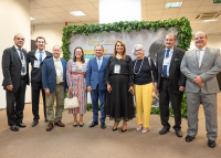 Seis homens vestidos de ternos claros e escuros e três mulheres, sendo duas delas trajando vestido e uma com calça comprida. Eles estão reunidos para um registro fotográfico.