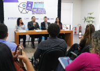 Ambiente de uma sala, com uma mesa ao fundo e quatro pessoas (duas mulheres e dois homens) voltadas para a plateia concedendo entrevista, tendo ao fundo painel com a marca do evento Mutirão Vaga Inclusiva de Trabalho