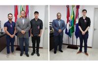 Duas fotos, sendo a primeira com dois homens vestidos de camisas e calças escuras e ladeados por um homem de terno cinza. Já a segunda há um homem de terno cinza um jovem de pel clara com roupa escura. Em ambas as fotos há três bandeiras .a