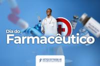 Homem negro de jaleco branco no centro da imagem de fundo azul e com o nome Dia do Farmacêutico; atrás do homem, um círculo com um cruz vermelha ao centro de um fundo branco em volto de outro círculo vermelho