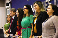 Cinco mulheres e um homem e um homem de pé em frente a uma bancada