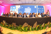 mesa com diversas autoridades a frente de um telão azul com letras brancas escrito XII Conferência Estadual da Advocacia