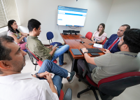 Grupo de pessoas, sendo duas mulheres e quatro homens, reunidos em frente a uma tela