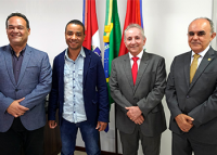 Quatro homens em pé utilizando, da esquerda para a direita, ternos cinza claro, azul marinho e chumbos, respectivamente.