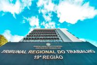 prédio cinza com uma placa na fachada de fundo azul com letras pratas escrito Tribunal Regional do Trabalho da 19ª Região