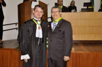 Dois homones brancos. Um usando toga e outro terno escuros. Eles usam também medalhas de honra ao mérito.