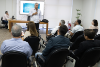 Homem branco de camisa branca com microfone na mão falando para um grupo de pessoas sentadas