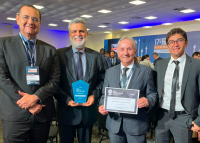 Na foto quatro homens sorridentes vestindo ternos e gravata trazendo nas maos a premiação recebida na solenidade