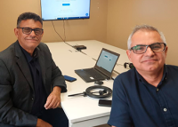 Na foto, um homem à esquerda com blazer preto e outro homem à direita com blusa azul marinho