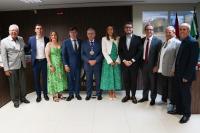 Homens e mulheres reunidos de pé para uma foto. Há dois homens de ternos na cor cinza claro  e seis de ternos escuros. As duas muleres estão de vestidos em tons de verde. Há um hoem usando uma medalha.