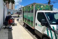 Caminhão barnco com baú verde, dois homens carregando uma estante para colocar dentro do caminhão