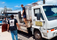 Há três homens trabalhando. Eles estão colocando móveis em caminhão branco.