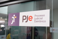 Porta de vidro adesivada com a logomarca da Justiça do Trabalho no lado esquerdo e as letras PJE ao centro, no lado direito está escrito Processo Judicial Eletrônico.