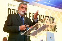 Presidente do TST, ministro Lélio Bentes, discursa usando um terno escuro, em frente a um painel amarelo 
