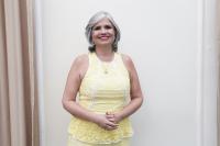 Mulher de pele morena, cabelos curtos e brancos, de vestido amarelo em pé de braços cruzados