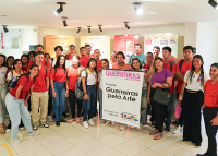 Vários jovens reunidos para uma foto. A maioria veste camiseta vermelha. Eles seguram um banner.