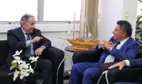 Dois homens de terno sentados em sofás diferente, conversam