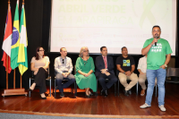 Grupo de pessoas, entre homens e mulheres, em cima de um palco a frente de um painel escrito Seminário Abril Verde em Arapiraca