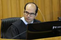 Homem branco, calvo, de cabelos pretos, óculos preto, vestindo toga preta