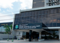 Fachada frontal com esquadrias pretas e janelas de vidro escuras. Há o Brasão da República em verde e amarelo a denominação do prédio em letras na cor branca, onde se lê Fórum Quintella Cavalcanti - Varas do Trabalho de Maceió.