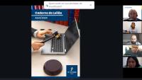 À esquerda, foto de um notebook aberto e, por cima dele, a duas masculinas, sendo que a mão direita está segurando um martelo todo preto com uma fita dourada em seu bojo, à direita, fotos de pessoas na sessão virtual do leilão, sendo quatro fotos de homens e uma foto de um mulher abaixo. 