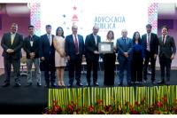 Na foto, 11 pessoas em pé, todos vestindo paletós ou roupas sociais; entre essas pessoas, três mulheres, uma de vestido bege outra de calça preta e blusa branca segurando o certificado com o ministro Balazeiro; à direita, uma mulher de calça preta e blusa azul.