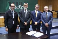 NA IMAGEM, QUATRO HOMENS USANDO PALETÓS; DA ESQUERDA À DIREITA, HOMEM CALVO, DE ÓCULOS,  USANDO PALETÓ ESCURO; HOMEM DE CABELO GRISALHO E BARBA GRISALHOS USANTO PALETÓ CINZA ESCURO; E DOIS HOMENS DE CABELOS LOUROS CLAROS E GRISALHOS USANDO PALETÓS AZUL ESCURO E CLARO, RESPECTIVAMENTE.