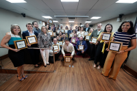 Fotos de um grupo de trinta pessoas, todas segurando um quadrinho de moldura dourado e sorrindo, demonstrando felicidade com o prêmio recebido