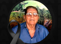 Homem idoso vestido de camisa azul. Há um laço preto na imgem que simboliza pesar por falecimento.