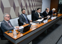 Sentados à mesa, cinco homens utilizando terno escuros