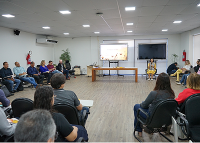 Vários alunos sentados de costa e, à frente, do lado direito, a professora sentada utilizando um vestido amarelo