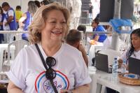 Mulher loira, de camisa branca cerca por pessoas fazendo atendimento público