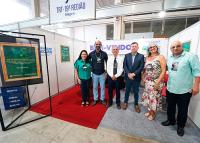 Grupo de homens e mulheres em pé dentro de um stand com a placa TRT-19