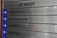 PLACA DE PVC NA COR CINZA ESCURO,  COM O NOME 2ª VARA DO TRABALHO DE MACEIÓ ESCRITO EM LETRAS PRETAS; ABAIXO DELE, DE CIMA PARA BAIXO, OS NOMES SALA DE AUDIÊNCIA, GABINETE DOS JUÍZES, BANHEIROS E SECRETARIA, TODOS NA COR PRETA. 