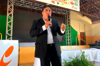 Homem moreno usando terno escuro falando ao microfone em um palco