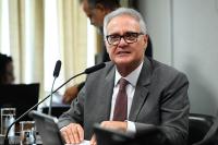 Homem branco, de óculos e cabelos brancos, vestindo terno cinza escuro e gravata roxa